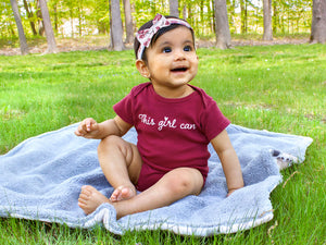 baby sits on blanket in grass and maroon onesie