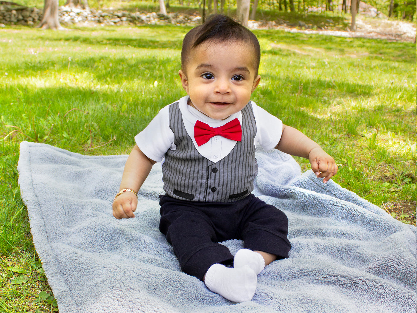 baby sits on blanket in grass in bowtie shirt